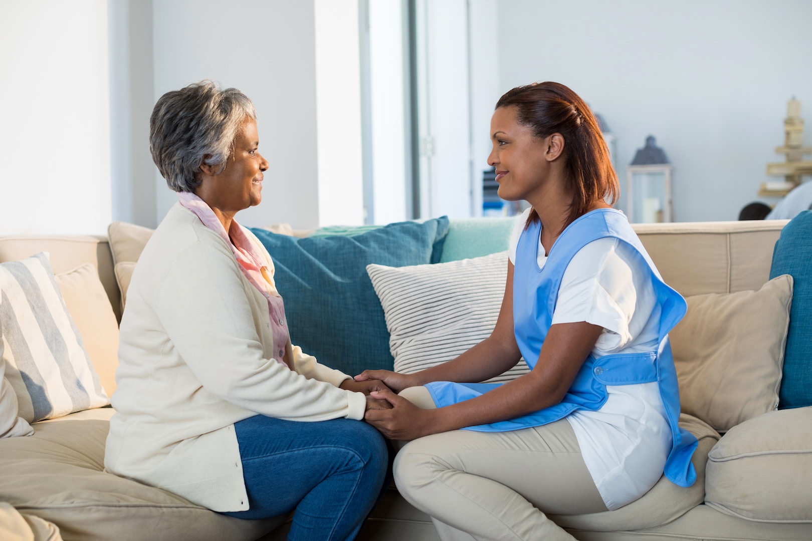 A caregiver holds hands with a senior woman in her living room.